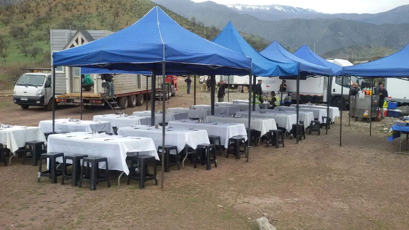 Hilera de coberturas con mesas montadas en terreno de montaña, con la cordillera nevada al fondo