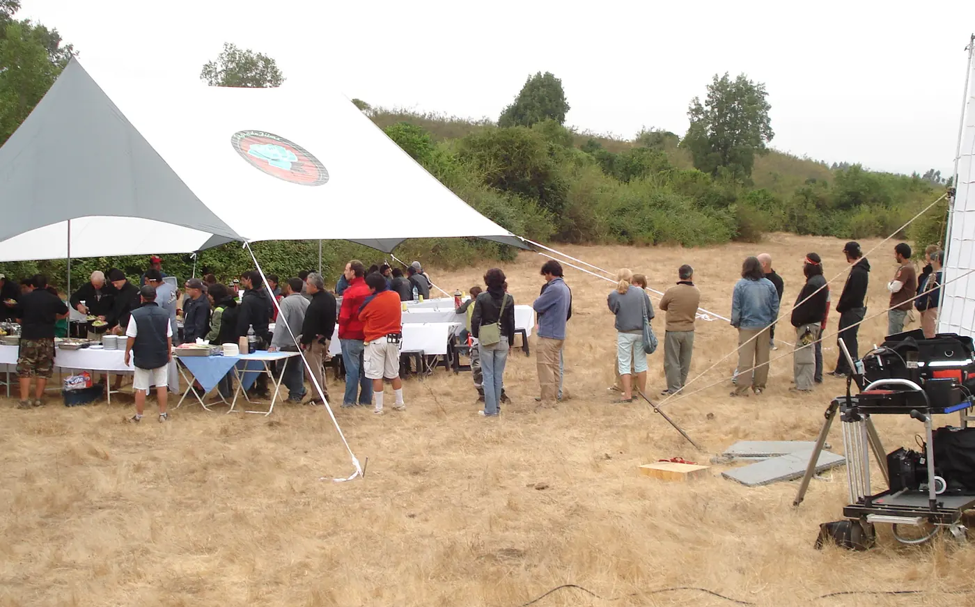 Carpa vela montada en terreno abierto con el equipo de producción sirviéndose