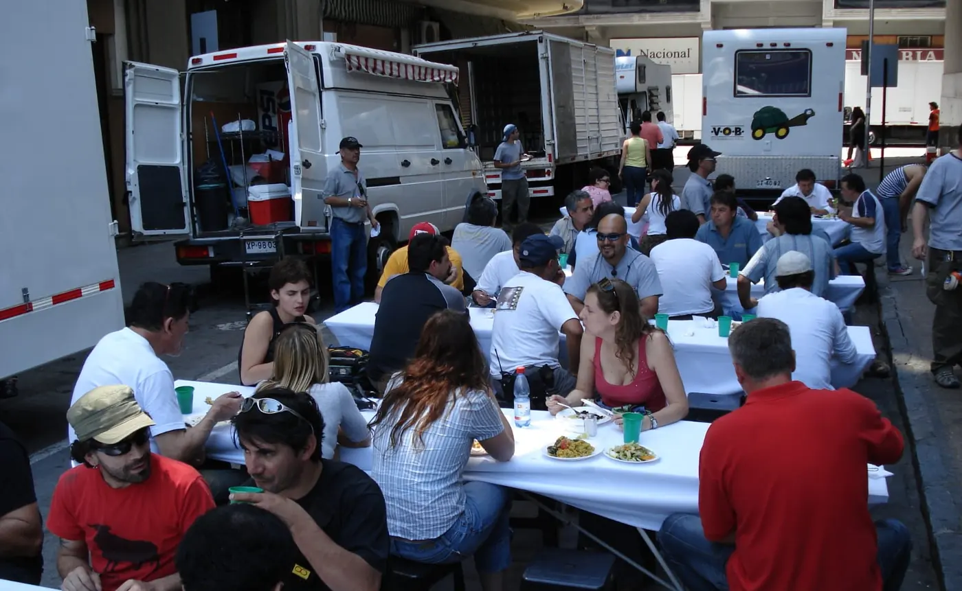 Equipo de producción almorzando en mesas largas junto a los camiones